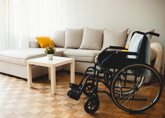 Empty wheelchair in the livingroom. Lonely and healthcare concept. Empty wheelchair dor a disable person with blue plaid on background of big couch with cushions in living-room