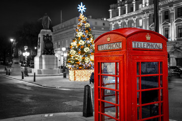 Fototapeta na wymiar Christmas in London with a red telephone booth in front of an illuminated Christmas Tree in Central London, UK, during night time