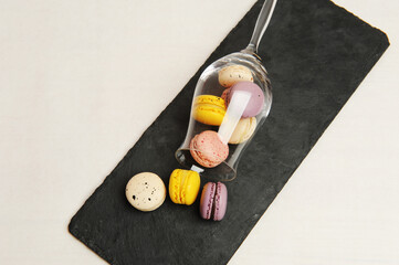 Colorful french mini macarons sprinkled from an overturned wine glass on slate board. White background.