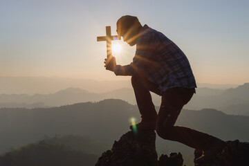 Silhouette humans pray to GOD while holding a crucifix symbol with a bright sunbeam on the mountain...