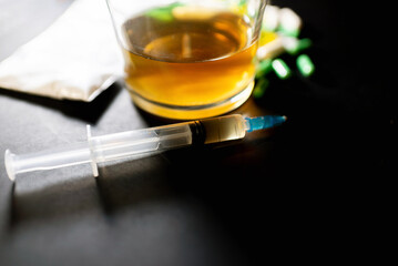 Hard drugs and alcohol on dark gray table. Alcohol pills syringe plastic bag powder of cocaine on table with shadow.Closeup.Copy space.