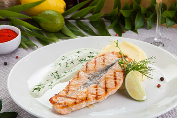 Grilled salmon fillet on a white plate, with mashed potatoes, cream sauce, and a slice of fresh lemon.