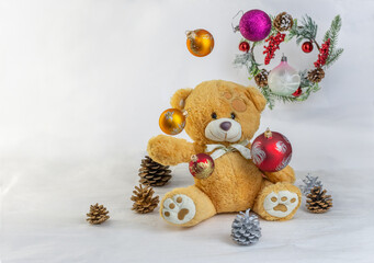 Christmas composition: a teddy bear juggles glass Christmas balls against the background of a Christmas wreath and pine cones. Selective focus