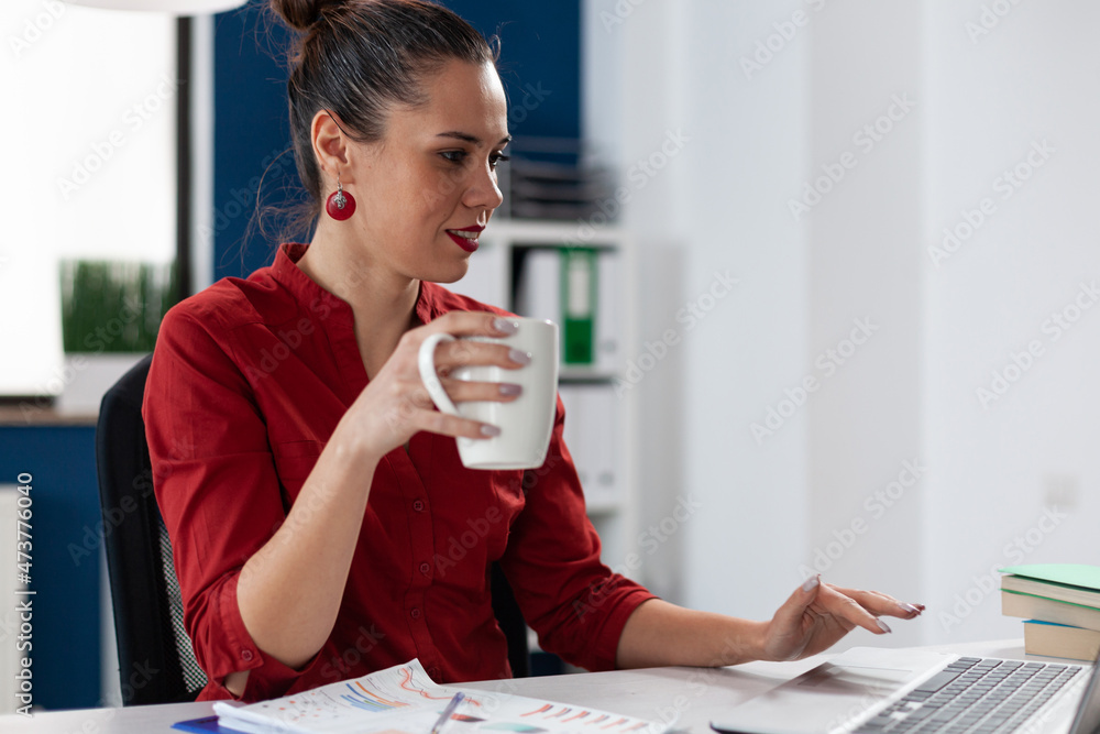 Aufkleber startup manager working casually on laptop while holding white cup. businesswoman in red shirt takin