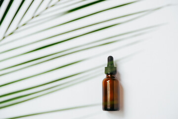 Essential oils on white background with palm leaves, mockup. Cosmetic medical beauty product in brown glass bottles with a pipette.