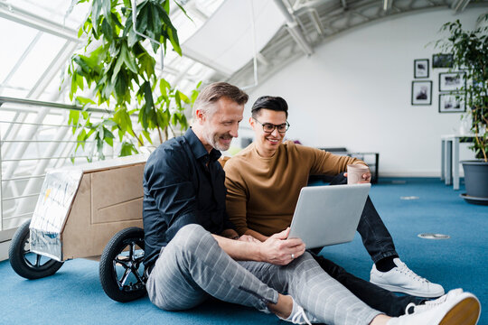 Male colleagues using laptop while sitting in creative office