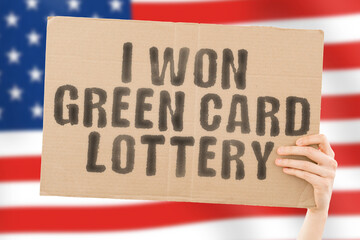 The phrase " I won green card lottery " on a banner in men's hand with blurred American flag on the background. Winner. Happy. Lucky. Power. Liberty. Freedom