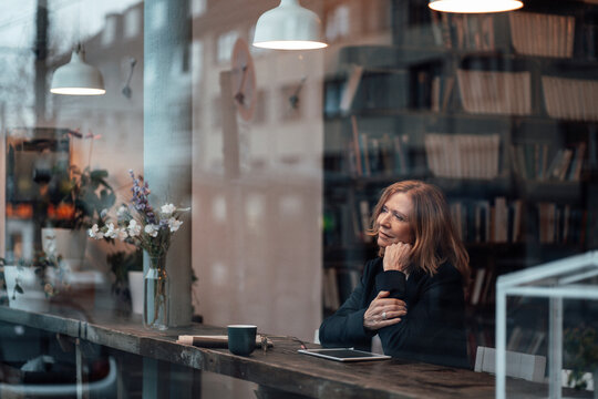 Thoughtful businesswoman sitting in cafe looking through glass window