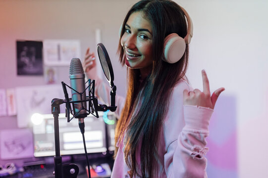 Smiling female singer wearing headphones gesturing while singing in studio