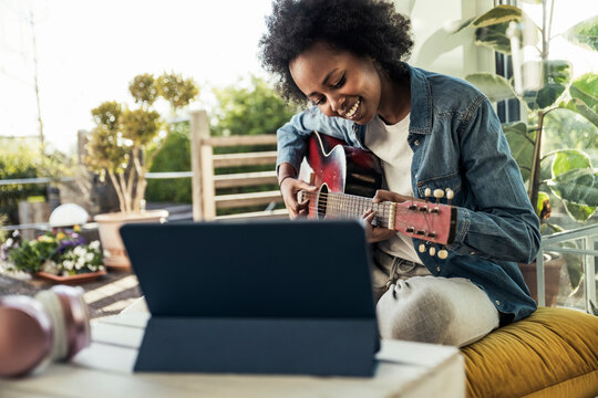 Young woman practicing guitar while e-learning through digital tablet at home