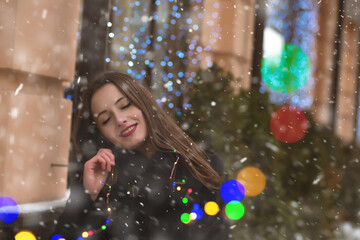 Pretty lady walking at the street with garlands during snowfall