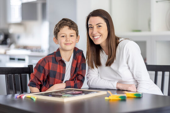 Smiling boy sitting by mother at table in kitchen