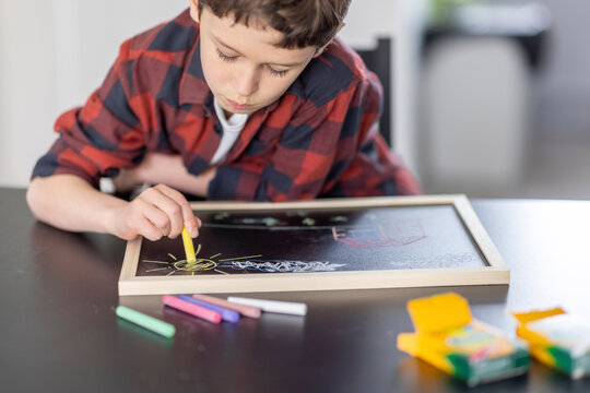 Boy drawing with colorful chalks on slate at home - Powered by Adobe