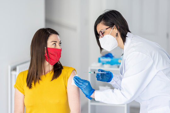Woman looking at female doctor giving COVID vaccine at clinic during pandemic