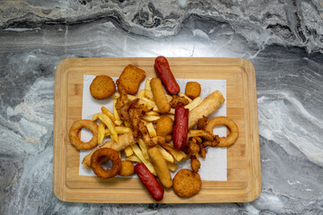 fast food meals : chicken nuggets and fried chicken, onion rings, french fries,  on wooden table