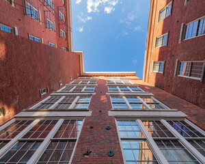 Looking skyward in an old mill factory that is a historic park and has been restored New England mill restored and now also living space, old windows symmetrical brick walls with star bolts  - obrazy, fototapety, plakaty