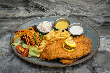 Chicken schnitzel and fried potatoes on plate over marble background. Top view, flat lay.
