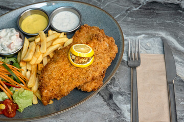 Chicken schnitzel and fried potatoes on plate over marble background. Top view, flat lay.