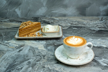 Cup of cappuccino and slice of cake with latte art on marble background