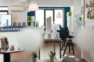 Empty architectural office with foam building model on table and computer screen with blueprints. Nobody in blue and white open space used by architect to design concept real estate.