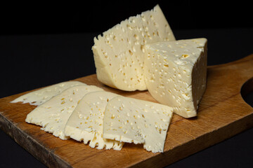 White cheese on a black background. Homemade white cheese on a wooden board. Traditional cuisine
