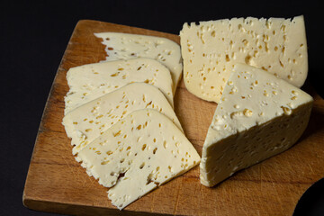 White cheese on a black background. Homemade white cheese on a wooden board. Traditional cuisine