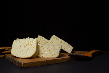 White cheese on a black background. Homemade white cheese on a wooden board. Traditional cuisine