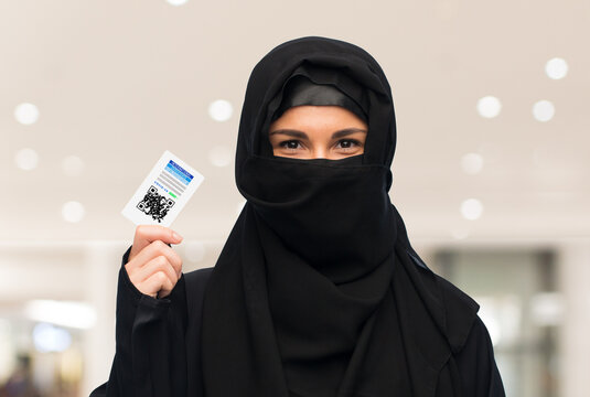 pandemic, health and people concept - woman in hijab with immunity passport qr code over shopping mall background