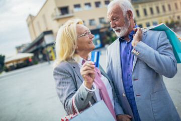 Happy senior couple walking with their shopping purchases on a sunny day using credit card.