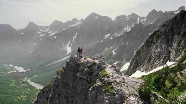 Flying around pair of hikers on the top of mountain. Aerial drone shot of man and woman travel with backpacks in the mountains. Valbona pass, Albanian Alps