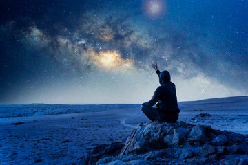 unknown person sitting on the rock hand up under the Milky Way at night celebrating or showing...