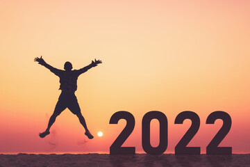 Silhouette man jumping with number like 2022 at tropical beach on sunset sky abstract background. Happy new year and holiday celebration concept.