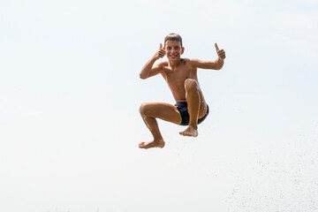 Happy ten years boy jumping in to water on wide river from the air. Summer vacation fun concept