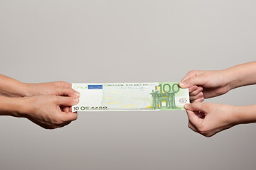 two pairs of human hands stretching a hundred euro bill