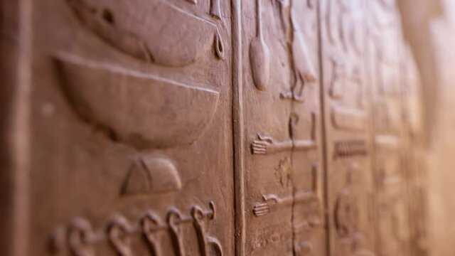 Close shot of Egyptian hieroglyphs on the wall in Hatshepsut temple. Antique stone wall with carved ancient Egyptian hieroglyphs. Shallow DOF
