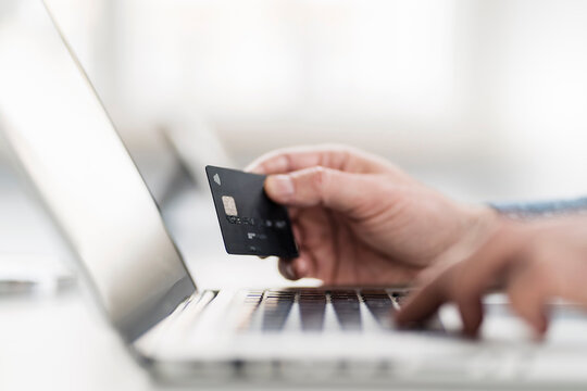 Hand of businessman using laptop while holding credit card at workplace