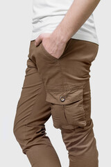 Side view of man wearing brown cargo pants with hand in pocket on grey background.