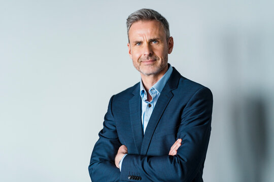 Male professional in businesswear with arms crossed in front of gray background