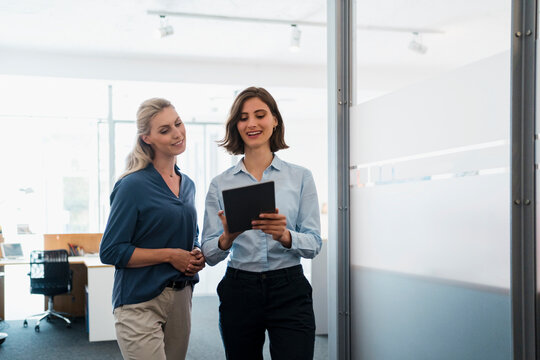 Young businesswoman discussing over digital tablet with female entrepreneur in office