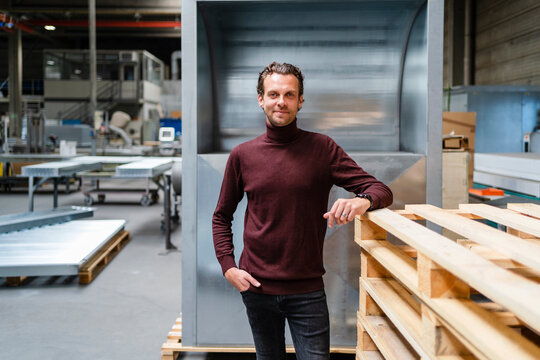 Male professional with hand in pocket standing by stack of wooden pallets