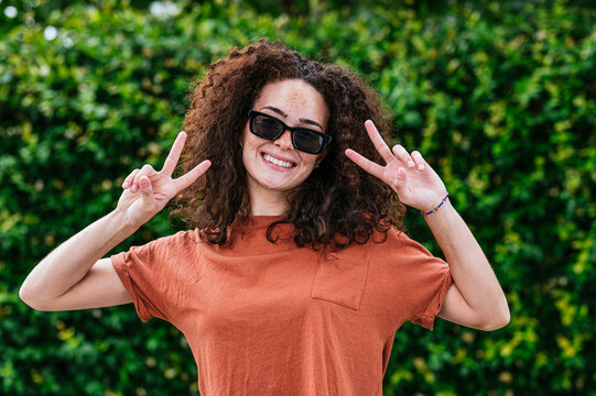 Smiling young woman wearing sunglasses gesturing peace sign