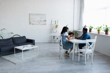 african american women and toddler girl in party caps playing wood blocks game in spacious living room