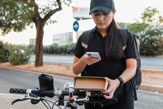 Young delivery woman with cycle scanning package through smart phone