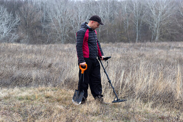 Fototapeta na wymiar a man with a metal detector and a shovel walks in a clearing near the forest