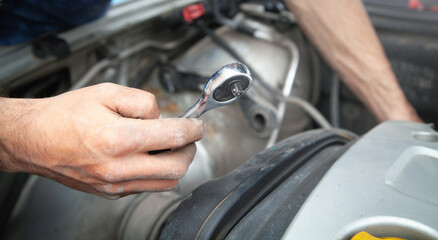 Mechanic repairing car with ratchet wrench.