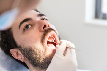 Female dentist with angled mirror examining male patient's teeth at medical clinic
