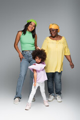 happy african american woman posing with stylish mom and daughter on grey