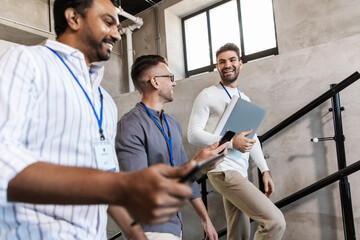 business, people and corporate concept - men with conference badges, folder, tablet pc computer and smartphone walking up office stairs