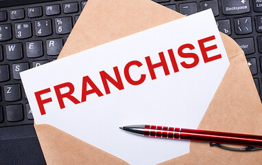 White card with the text FRANCHISE in a craft envelope on a work desk with a modern laptop keyboard...