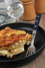 Portion de gratin de pommes de terre servie dans une assiette avec une fourchette et un verre d'eau